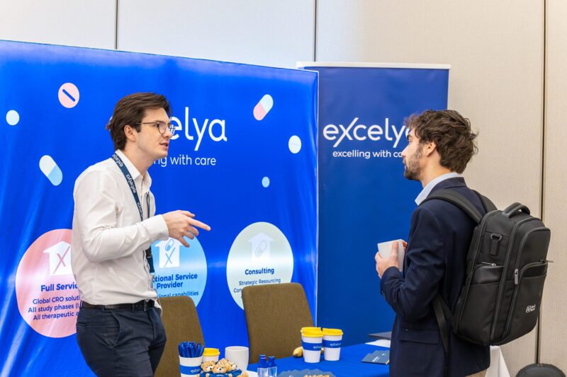 Excelya representative discussing clinical research services with attendee at Excelya booth during clinical research conference